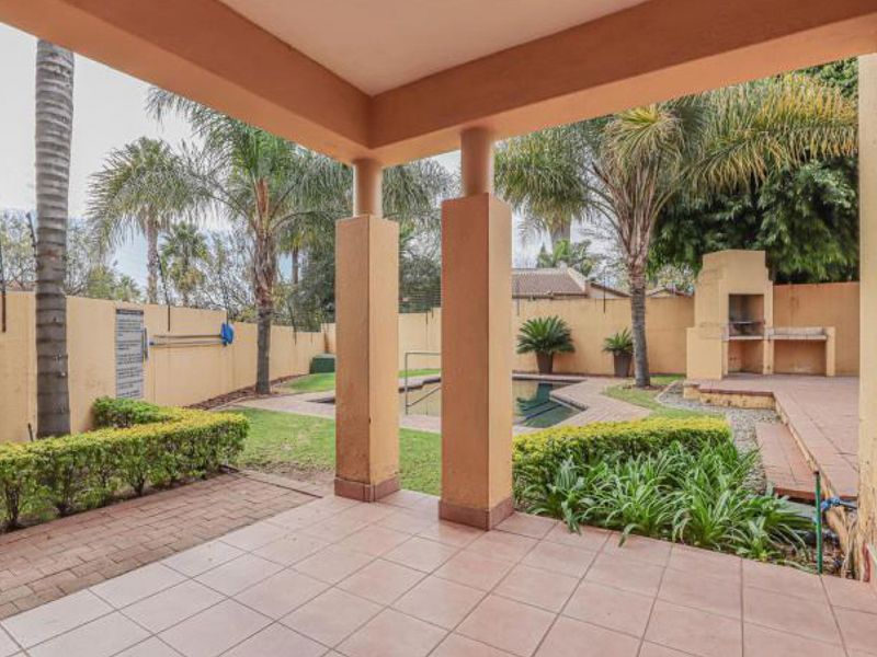 Covered patio area overlooking a private garden with a swimming pool and built-in masonry braai, ideal for outdoor entertaining.
