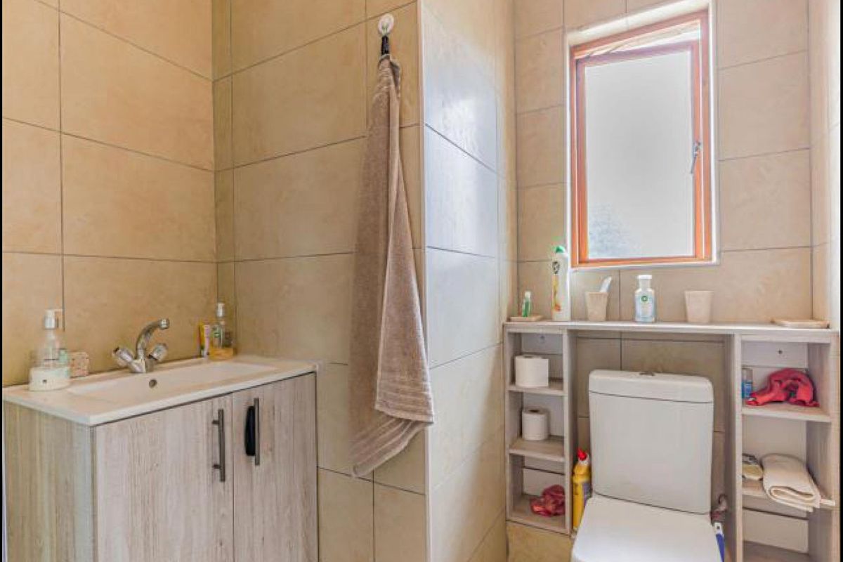 A compact bathroom featuring a modern vanity with basin, a toilet with integrated shelving, and neutral wall tiling.