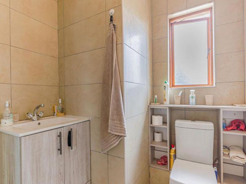 A compact bathroom featuring a modern vanity with basin, a toilet with integrated shelving, and neutral wall tiling.