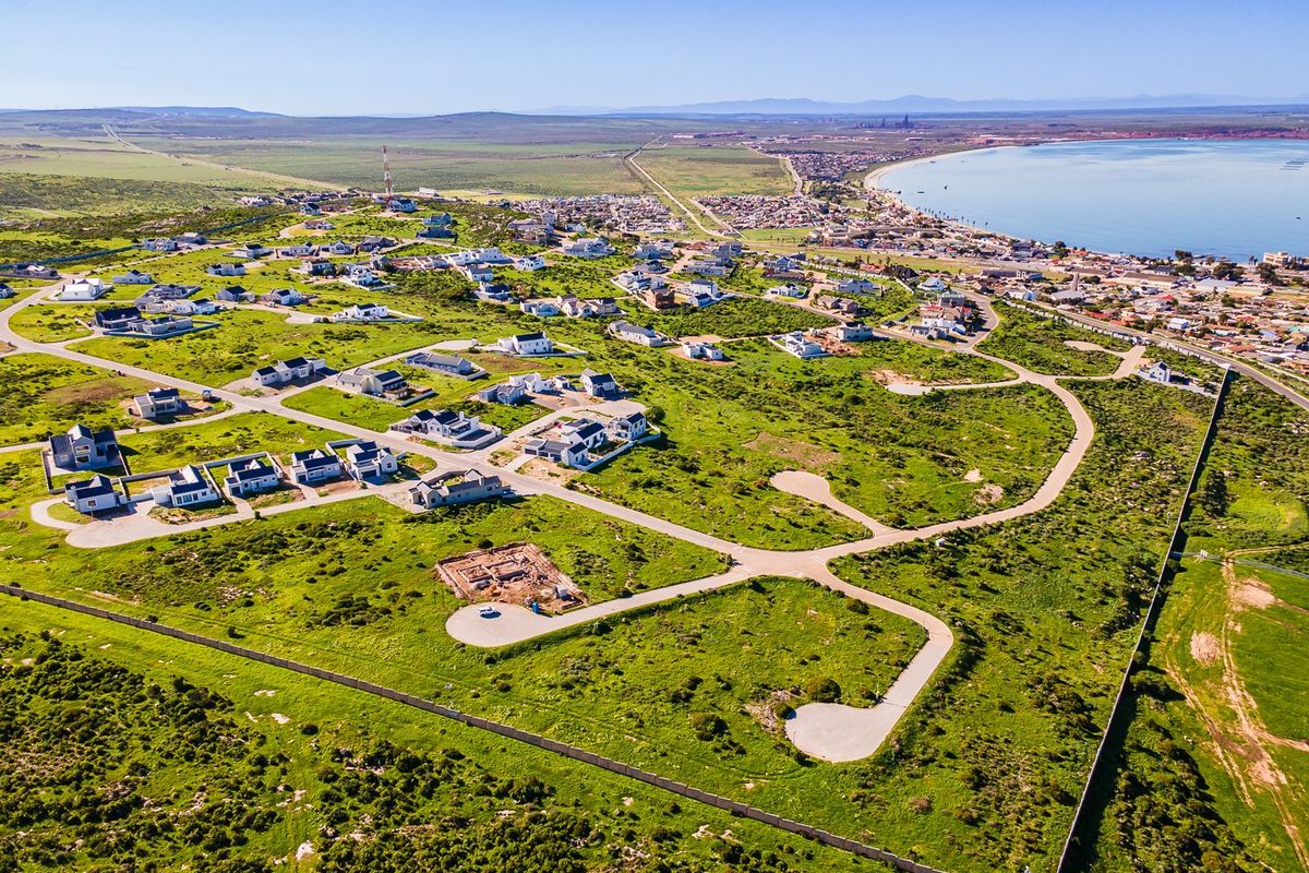 Aerial view of a residential development site featuring paved roads, perimeter fencing, and surrounding coastal landscape.