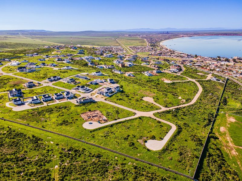 Aerial view of a residential development site featuring paved roads, perimeter fencing, and surrounding coastal landscape.