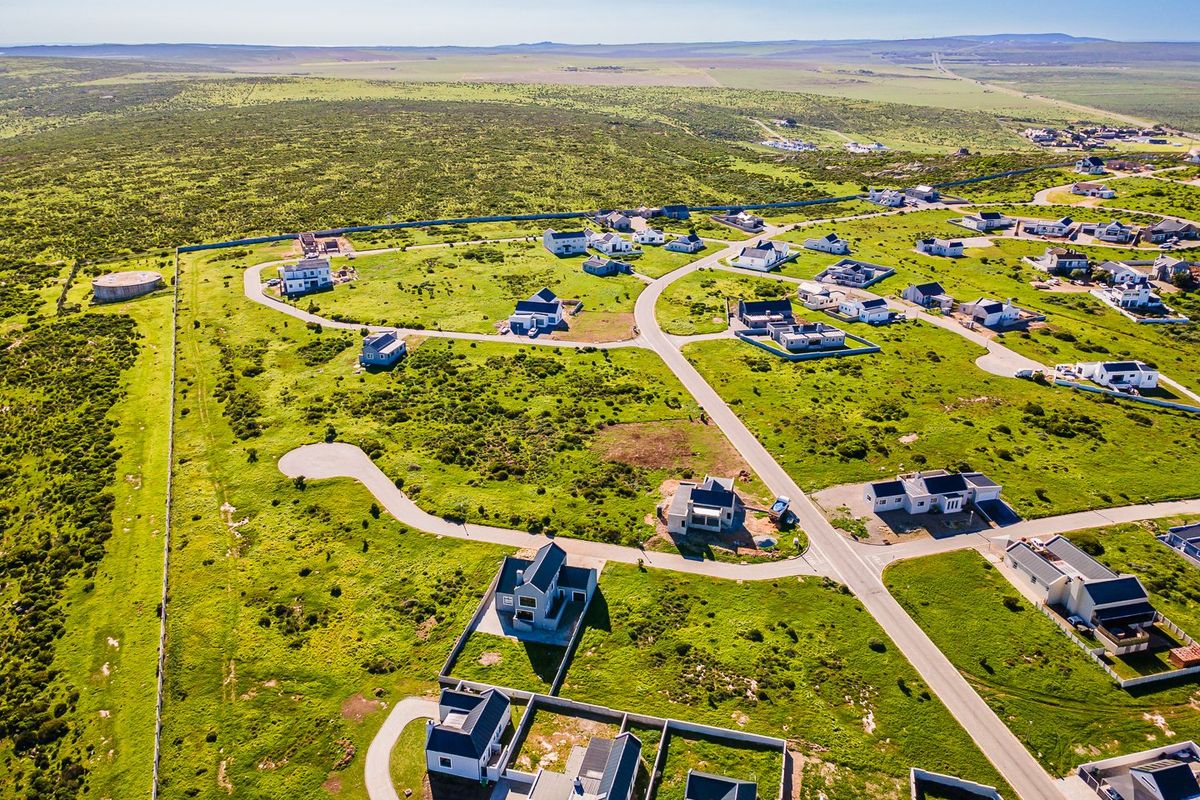 An aerial view of a residential development featuring paved roads, boundary walls, and multiple detached homes set within a natural landscape.