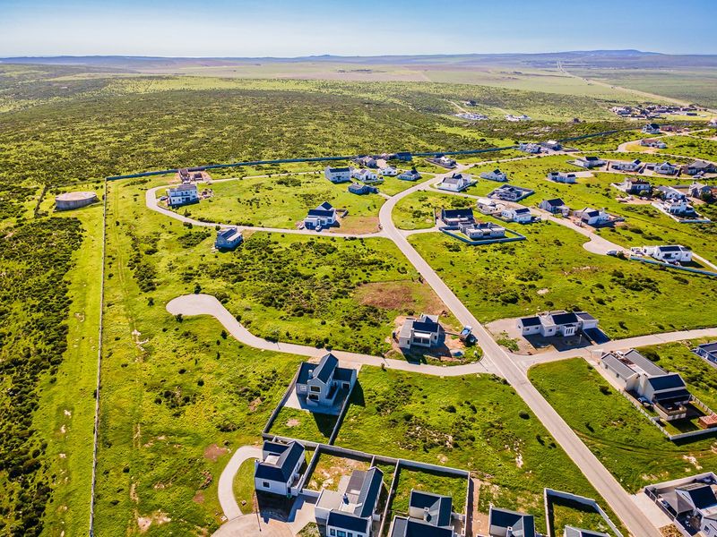 An aerial view of a residential development featuring paved roads, boundary walls, and multiple detached homes set within a natural landscape.