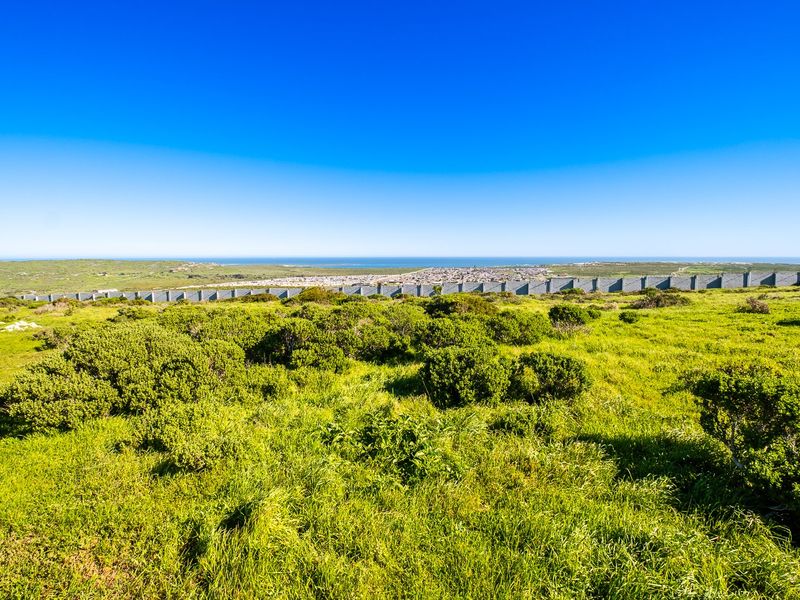 A scenic view overlooking a grassy landscape with a distant coastal town and ocean horizon, featuring a long boundary wall.