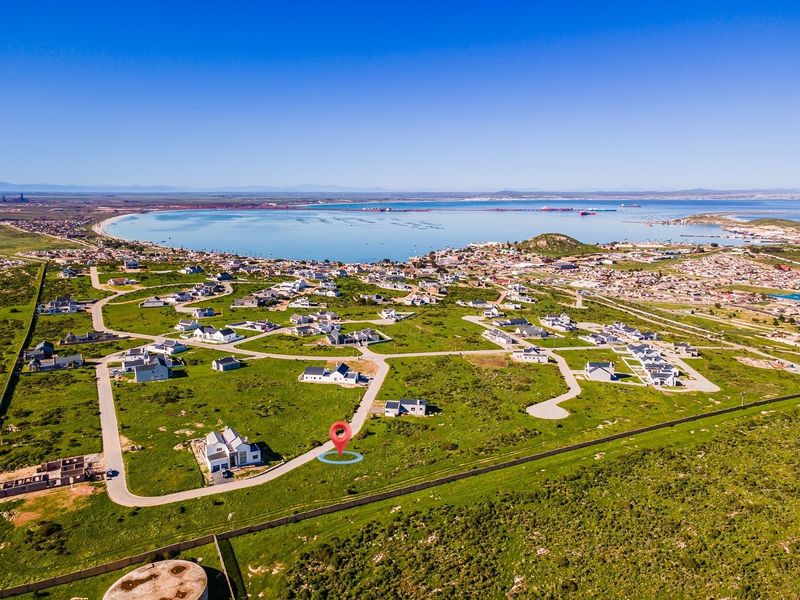 Aerial view of a residential estate development featuring paved roads and coastal proximity, highlighting the location of the vacant land plot.