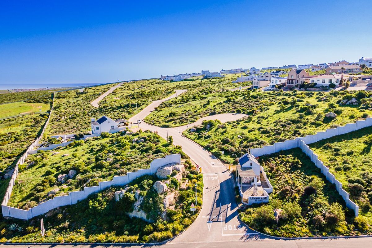 Aerial view of the Hoogland Estate entrance, featuring a security gatehouse, perimeter walling, and paved access roads within a landscaped residential development.