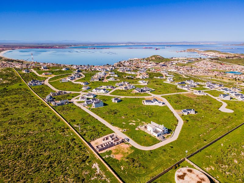 An aerial view of a residential development area featuring paved roads, established plots, and proximity to the coastline.