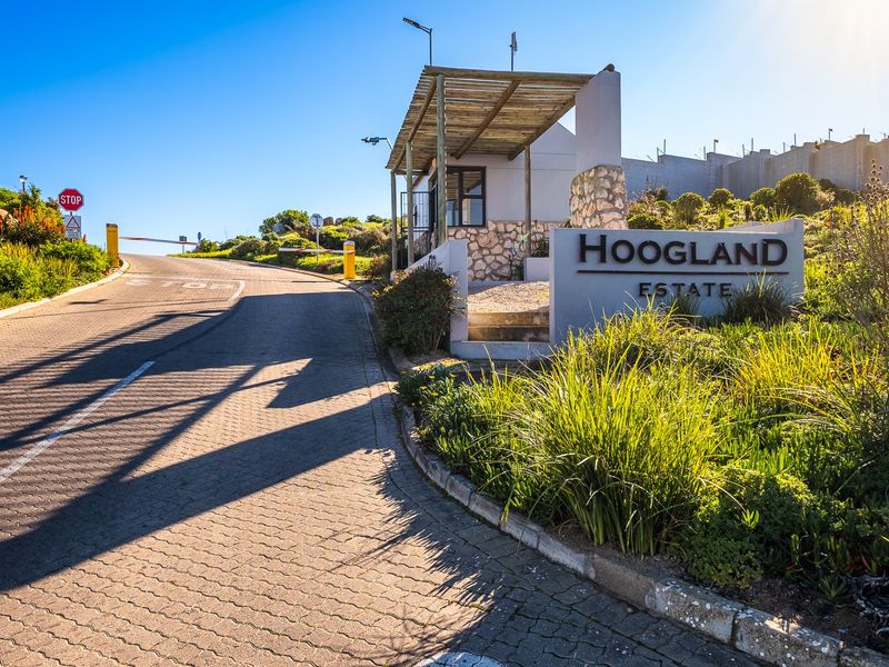 The entrance to Hoogland Estate featuring a paved driveway, security gatehouse, and perimeter wall, providing a secure and well-maintained access point to the property.