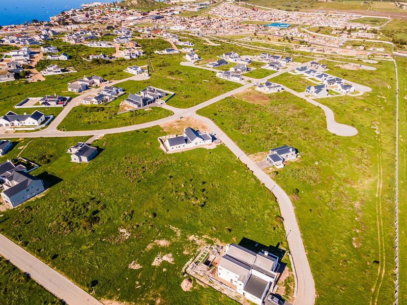 An aerial view of a residential development featuring vacant plots and established homes near the coastline.