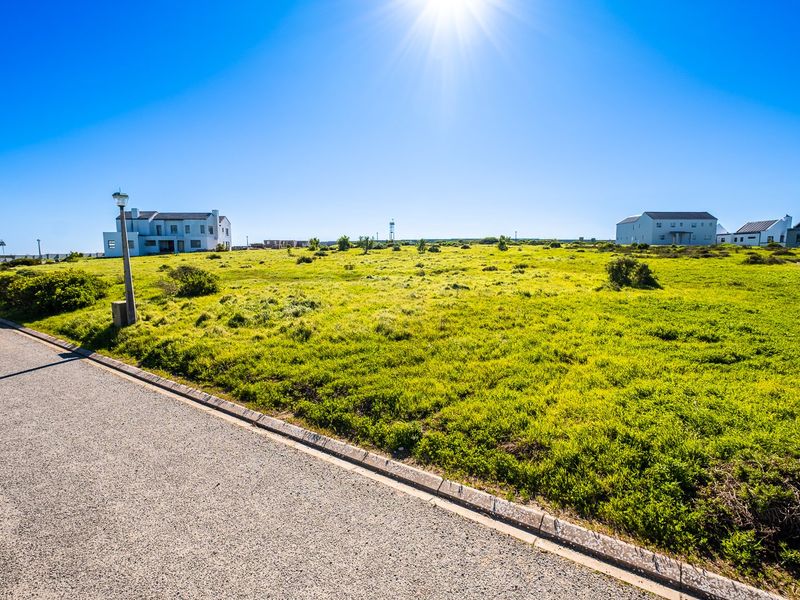 A vacant residential plot of land featuring a grassy landscape, adjacent to an asphalt road with a street lamp.