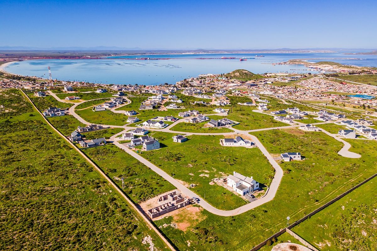 An aerial view of a residential development area featuring paved roads, established plots, and proximity to the coastline.