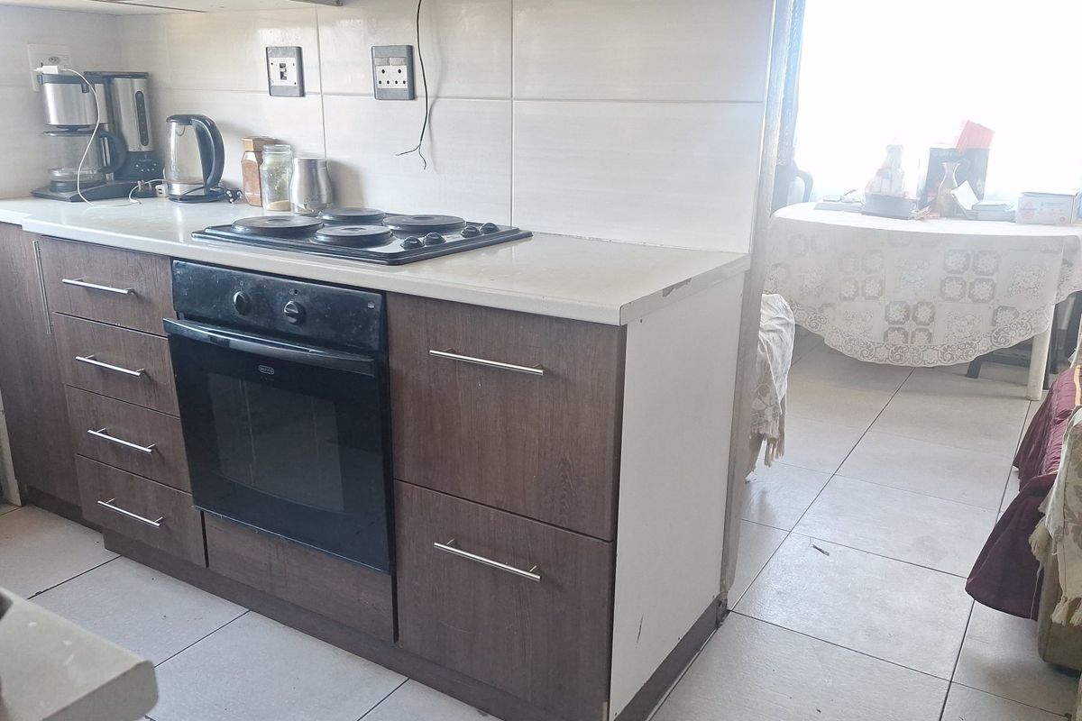 A functional kitchen area featuring dark wood-finish cabinetry, a built-in oven with electric hob, and tiled splashbacks, adjacent to a dining space.