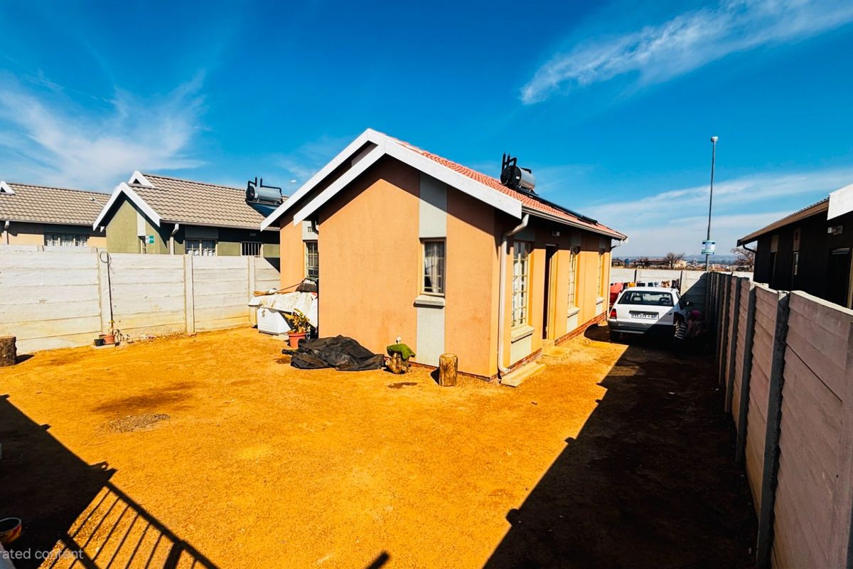 Rear view of a detached house featuring a tiled roof, solar water heater, and a large unpaved yard enclosed by precast concrete boundary walls.