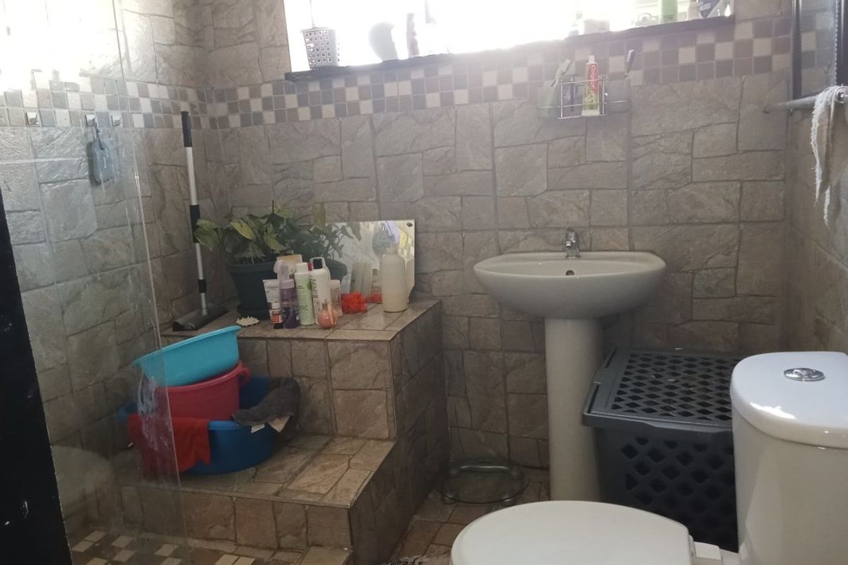 A functional bathroom featuring tiled wall finishes, a pedestal basin, a toilet, and a glass-enclosed shower area.