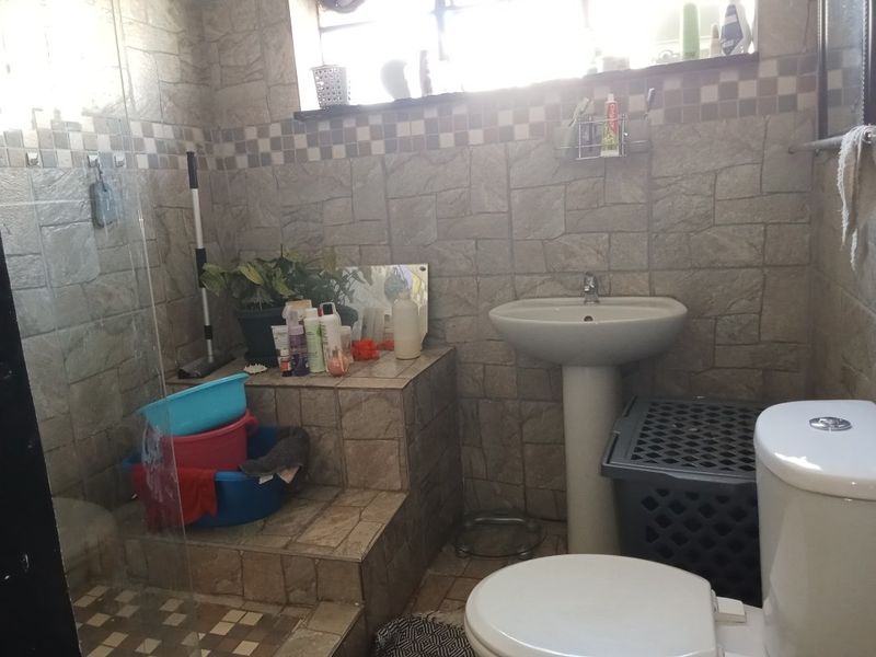 A functional bathroom featuring tiled wall finishes, a pedestal basin, a toilet, and a glass-enclosed shower area.