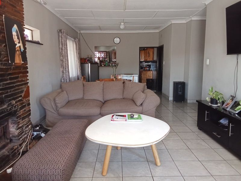 Spacious living room featuring tiled flooring and a prominent brick fireplace, offering a comfortable layout with direct access to the kitchen area.