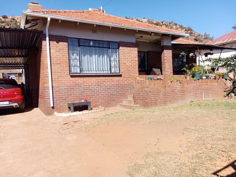 A traditional face brick house featuring a covered carport, raised front patio, and classic steel-framed windows, set on a residential plot.