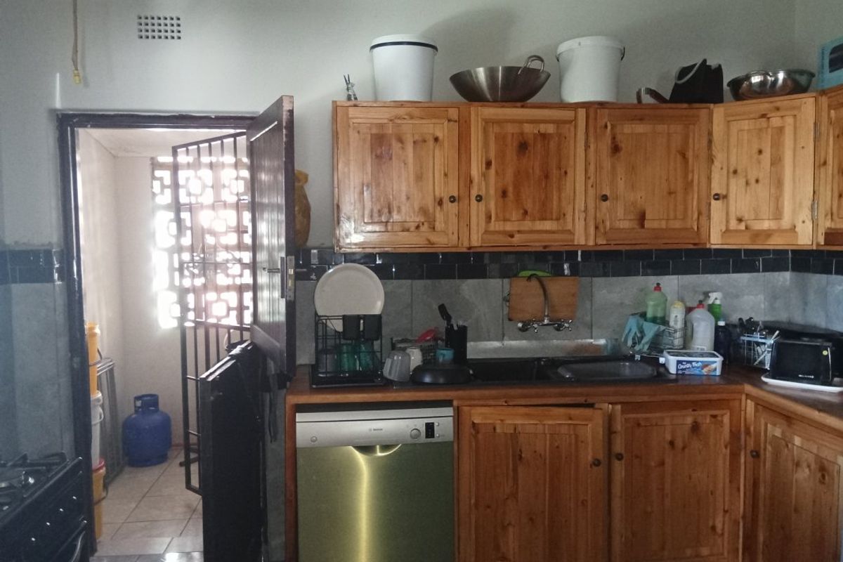 A functional kitchen featuring wooden cabinetry, a double sink, and an integrated dishwasher, with an adjacent utility area visible through a security gate.
