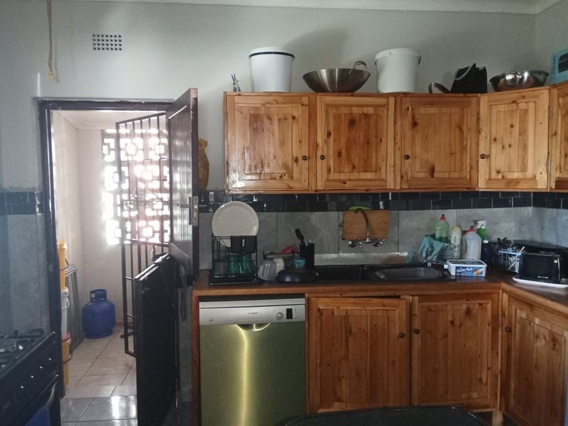 A functional kitchen featuring wooden cabinetry, a double sink, and an integrated dishwasher, with an adjacent utility area visible through a security gate.