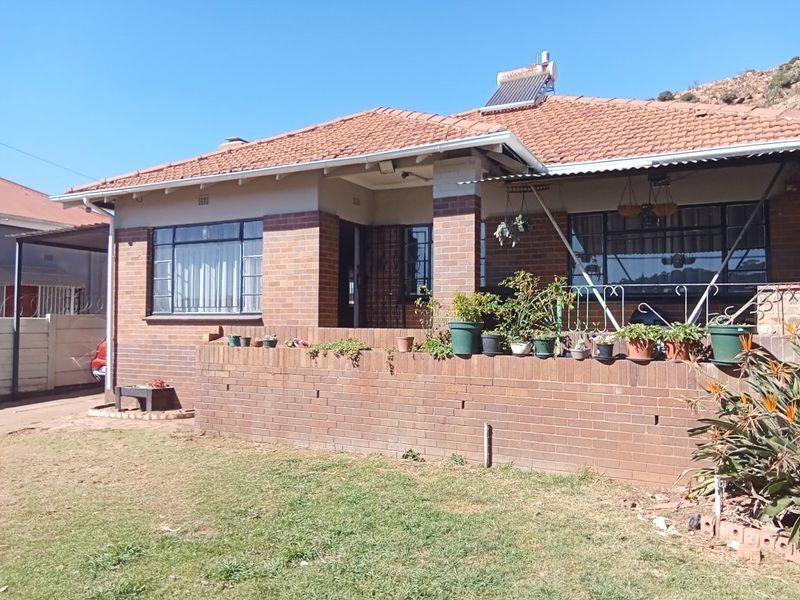 Front view of a single-story brick house featuring a tiled roof, solar water heater, and a low brick boundary wall with a covered porch area.