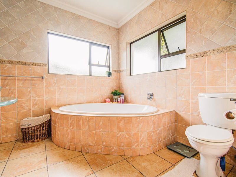 A functional bathroom featuring a built-in corner bathtub, ceramic tiling throughout, and a standard toilet, illuminated by natural light from two casement windows.