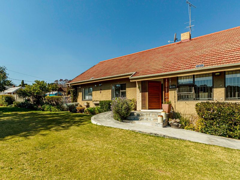 A well-maintained single-story brick house featuring a tiled roof, a concrete walkway leading to the entrance, and a spacious front lawn.