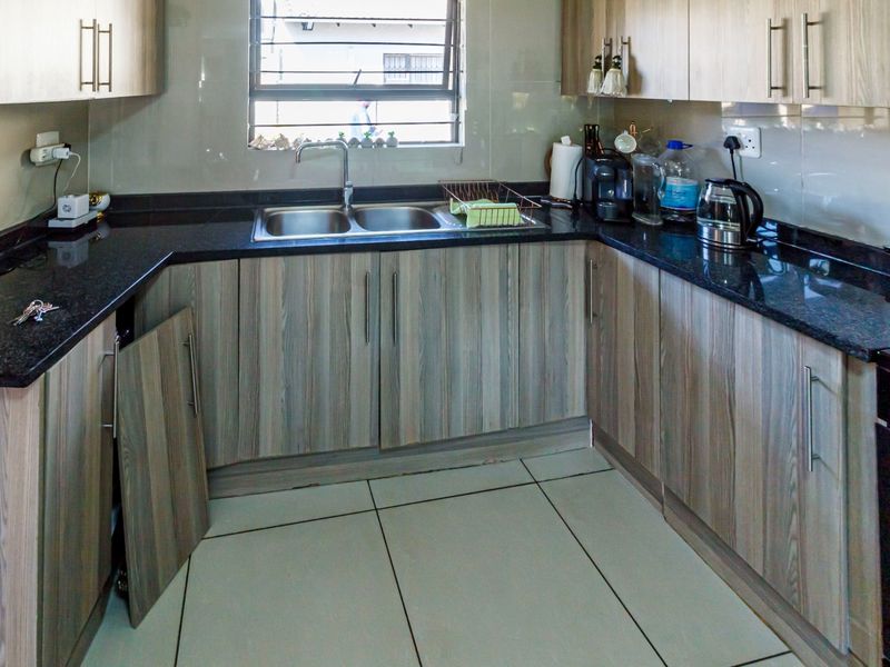 A functional kitchen featuring granite countertops, tiled backsplash, and wood-finish cabinetry, currently requiring minor repairs to a detached cabinet door.