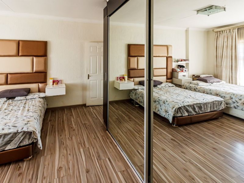 Spacious bedroom featuring wood-look laminate flooring, a large mirrored built-in wardrobe, and neutral wall finishes.