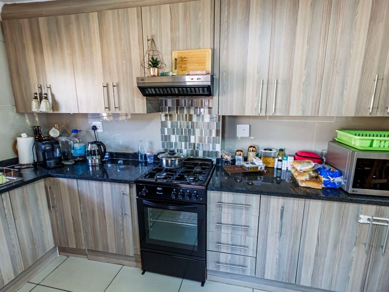 A functional kitchen featuring wood-look laminate cabinetry, dark granite countertops, a gas stove with extractor fan, and a decorative tiled backsplash.