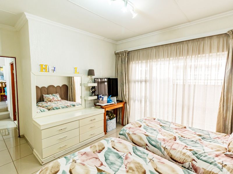 A well-lit bedroom featuring tiled flooring, ceiling cornicing, and a large sliding glass door with curtain tracks providing access to the exterior.