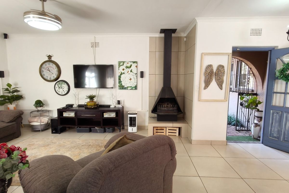 A spacious living room featuring tiled flooring, a modern freestanding fireplace, and a ceiling fan, with direct access to an outdoor area.