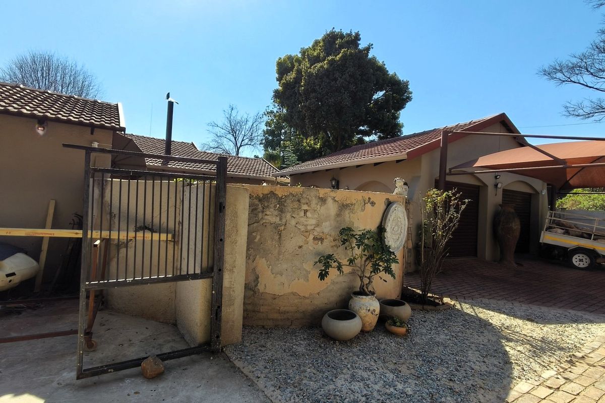 Rear exterior view showing a paved driveway, carport, garage access, and a weathered boundary wall requiring maintenance.