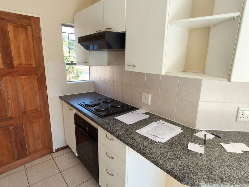 A functional kitchen featuring white cabinetry, granite-look laminate countertops, a built-in oven with hob, and tiled splashbacks.