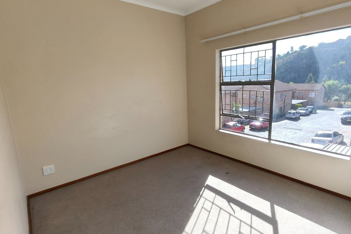 An empty bedroom featuring carpeted flooring, a large window with security bars, and neutral wall finishes.