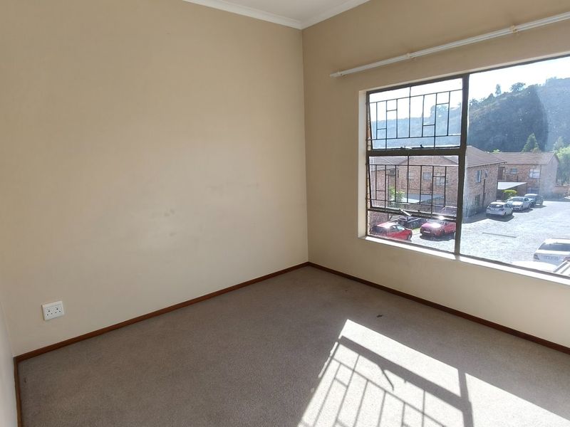 An empty bedroom featuring carpeted flooring, a large window with security bars, and neutral wall finishes.