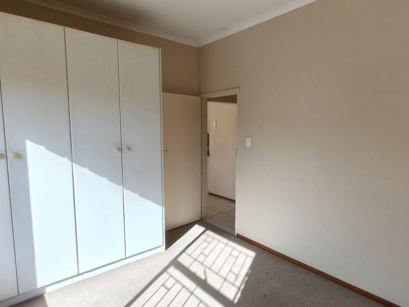A vacant bedroom featuring built-in cupboards, carpeted flooring, and neutral wall finishes, offering a blank canvas for potential updates.