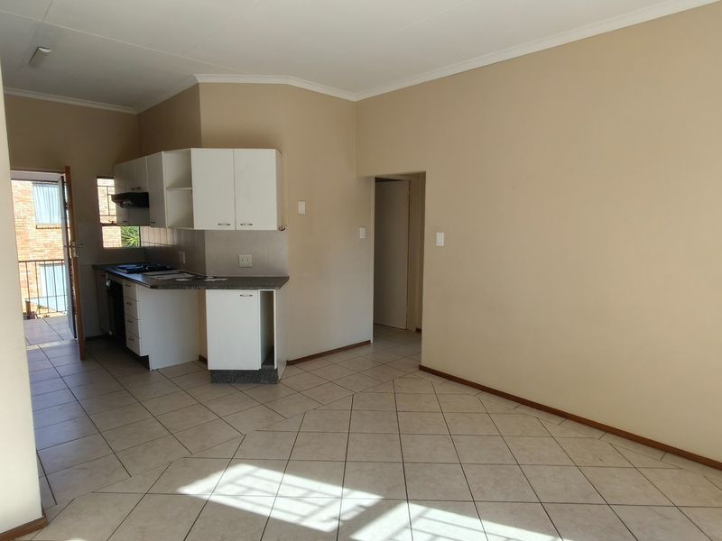 An open-plan living and kitchen area featuring tiled flooring, neutral walls, and functional built-in kitchen cabinetry with a hob and extractor fan.