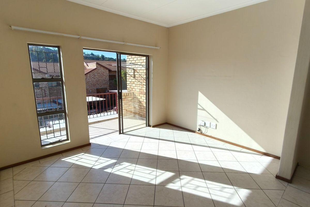 An empty, sunlit living area featuring neutral tiled flooring and direct access to a private balcony through sliding glass doors.