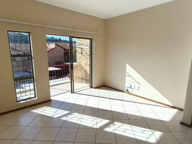 An empty, sunlit living area featuring neutral tiled flooring and direct access to a private balcony through sliding glass doors.