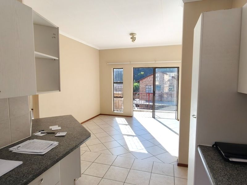 An open-plan kitchen and living area featuring tiled flooring, built-in cabinetry with granite countertops, and a sliding door leading to a balcony.