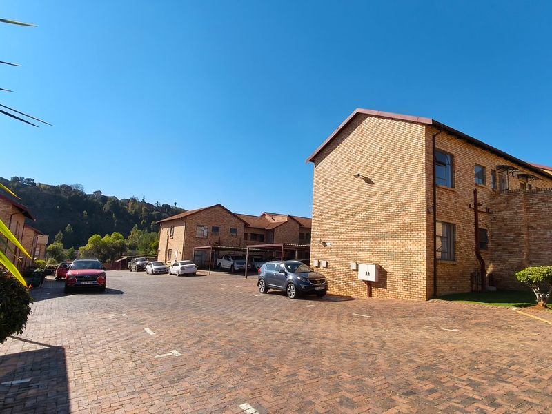 Exterior view of a face brick apartment complex featuring a paved driveway and covered parking areas.