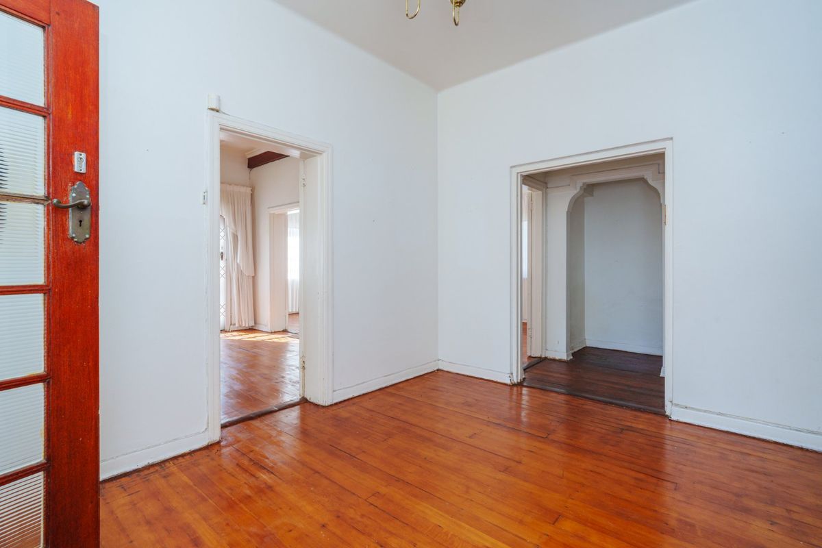 An empty living area featuring polished hardwood flooring and classic architectural archways connecting to adjacent rooms.