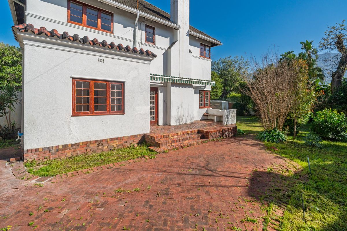 Rear exterior view of the house featuring a brick paved patio, built-in masonry bench, and a retractable awning against a white rendered facade.