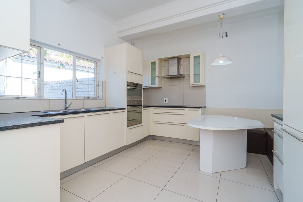 Functional kitchen featuring cream cabinetry, dark stone countertops, built-in oven, extractor fan, and tiled flooring with an integrated breakfast nook area.