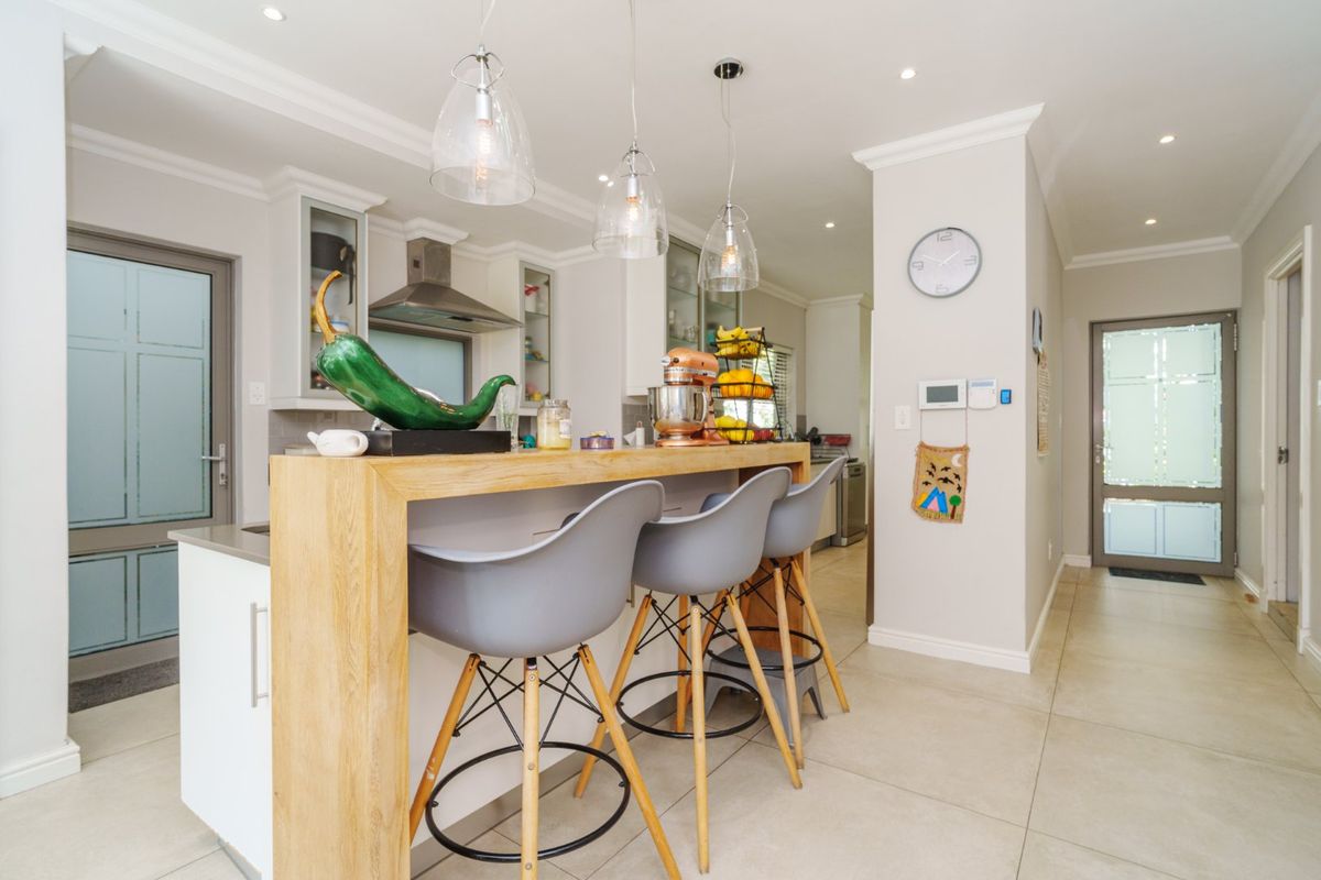 Modern kitchen featuring a central island with stone countertops, pendant lighting, and tiled flooring, seamlessly integrated into an open-plan living space.