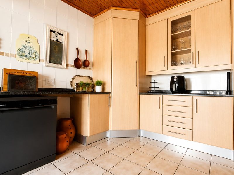 A functional kitchen featuring light wood cabinetry, dark granite countertops, tiled backsplash, and warm timber ceiling paneling.