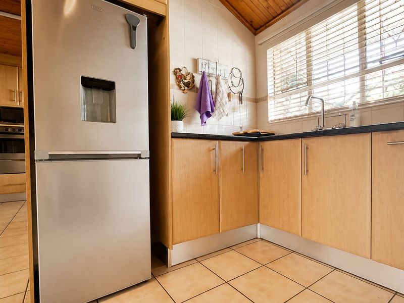 A functional kitchen featuring light wood cabinetry, dark laminate countertops, tiled flooring, and a warm timber-paneled ceiling with natural light from the window.