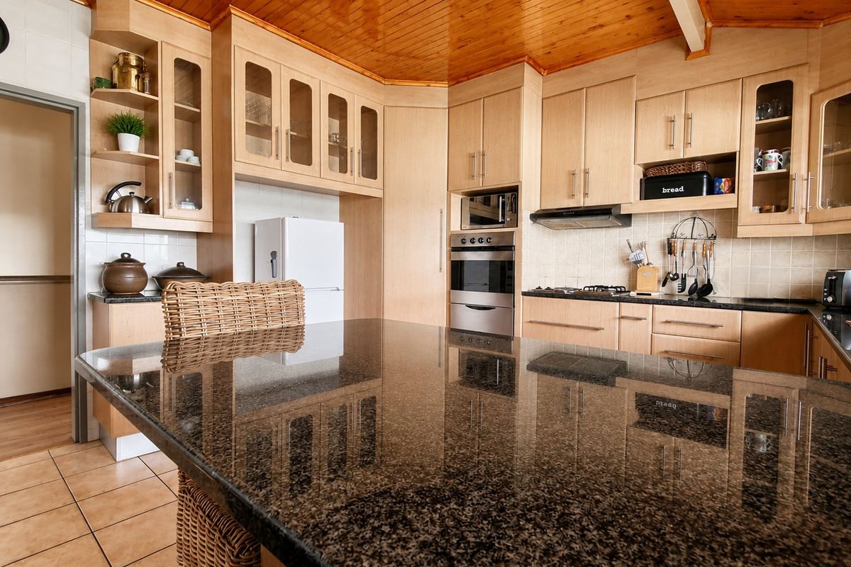 A well-maintained kitchen featuring light wood cabinetry, granite countertops, a built-in oven, and a distinctive timber-paneled ceiling.