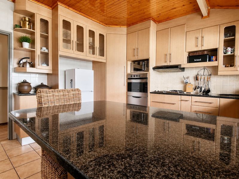 A well-maintained kitchen featuring light wood cabinetry, granite countertops, a built-in oven, and a distinctive timber-paneled ceiling.