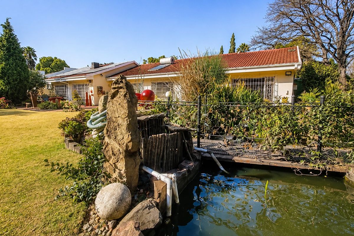 Rear view of the property featuring a landscaped garden, a pond with a small bridge, and a tiled roof house with security bars.